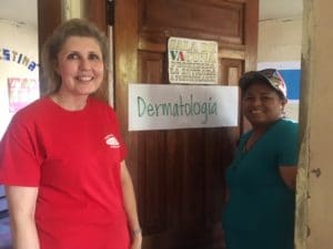 Photo of Mellissa Binney smiling with a person in front of a door labeled "dermatologia."